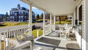 A covered porch with wicker chairs and a bench, overlooking a street and a large building. - Biking Trails, Fishing, Parks & More! Poconos Home (White Haven)