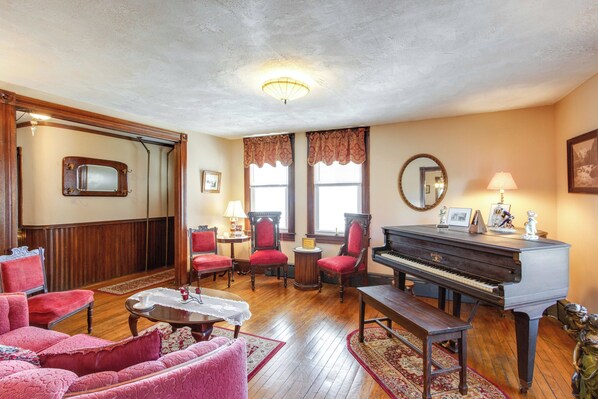 A spacious living room with a grand piano, red upholstered chairs, a wooden coffee table, and a large mirror. - Biking Trails, Fishing, Parks & More! Poconos Home (White Haven)