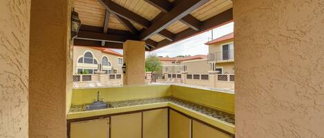 A small, enclosed kitchen area with a sink and tiled backsplash, wooden ceiling beams, and a view of neighboring buildings.