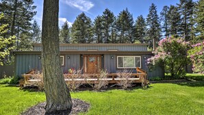 A single-story house with a deck, surrounded by a well-maintained lawn and tall trees. - Spacious Whitefish Getaway: Hike, Ski, Bike & More (Whitefish)
