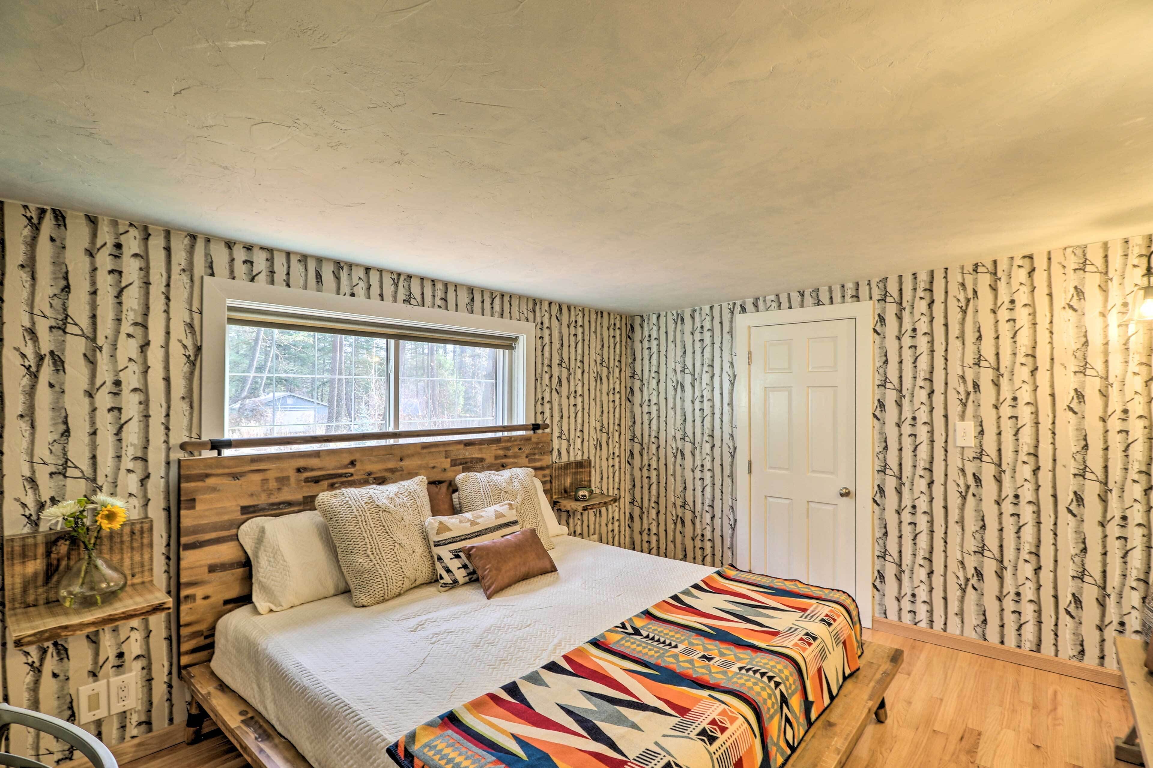 A bedroom with a wooden headboard, a window, a door, and a patterned wallpaper.