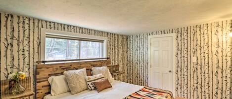 A bedroom with a wooden headboard, a window, a door, and a patterned wallpaper.