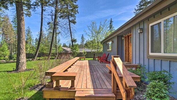 A wooden deck with picnic tables and chairs, surrounded by trees and a house. - Spacious Whitefish Getaway: Hike, Ski, Bike & More (Whitefish)