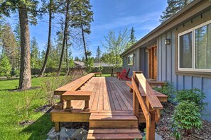 Une terrasse en bois, agrémentée de tables et de chaises pour pique-niquer, entourée d’arbres et d’une maison.