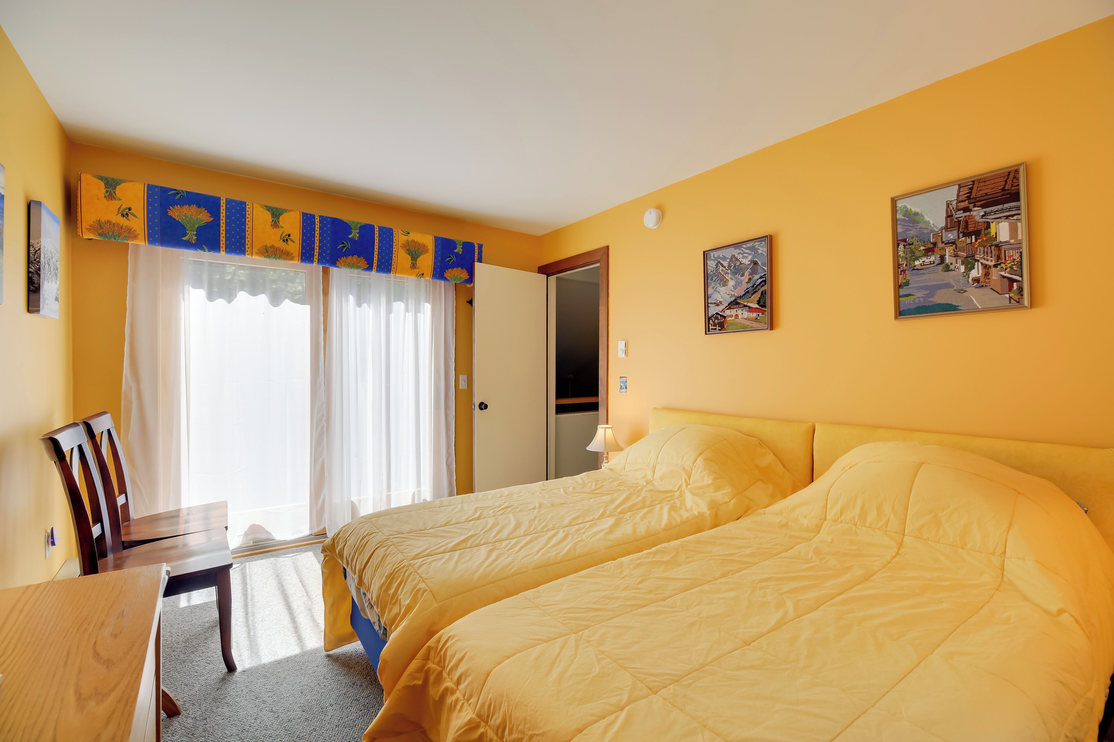 Une chambre d’hôtel avec deux lits, un bureau, une chaise et une fenêtre avec des rideaux.
