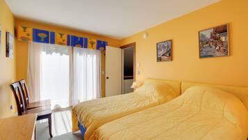 A hotel room with two beds, a desk, a chair, and a window with curtains.