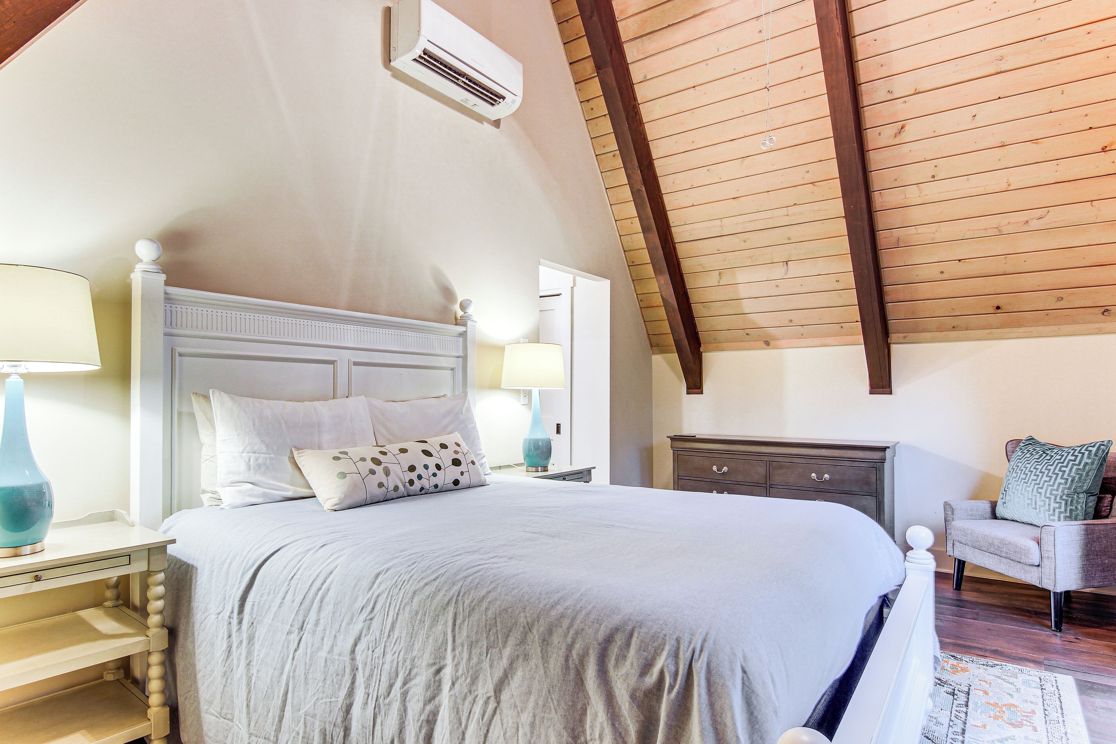 A bedroom with a large bed, two bedside tables with lamps, a dresser, and a chair.