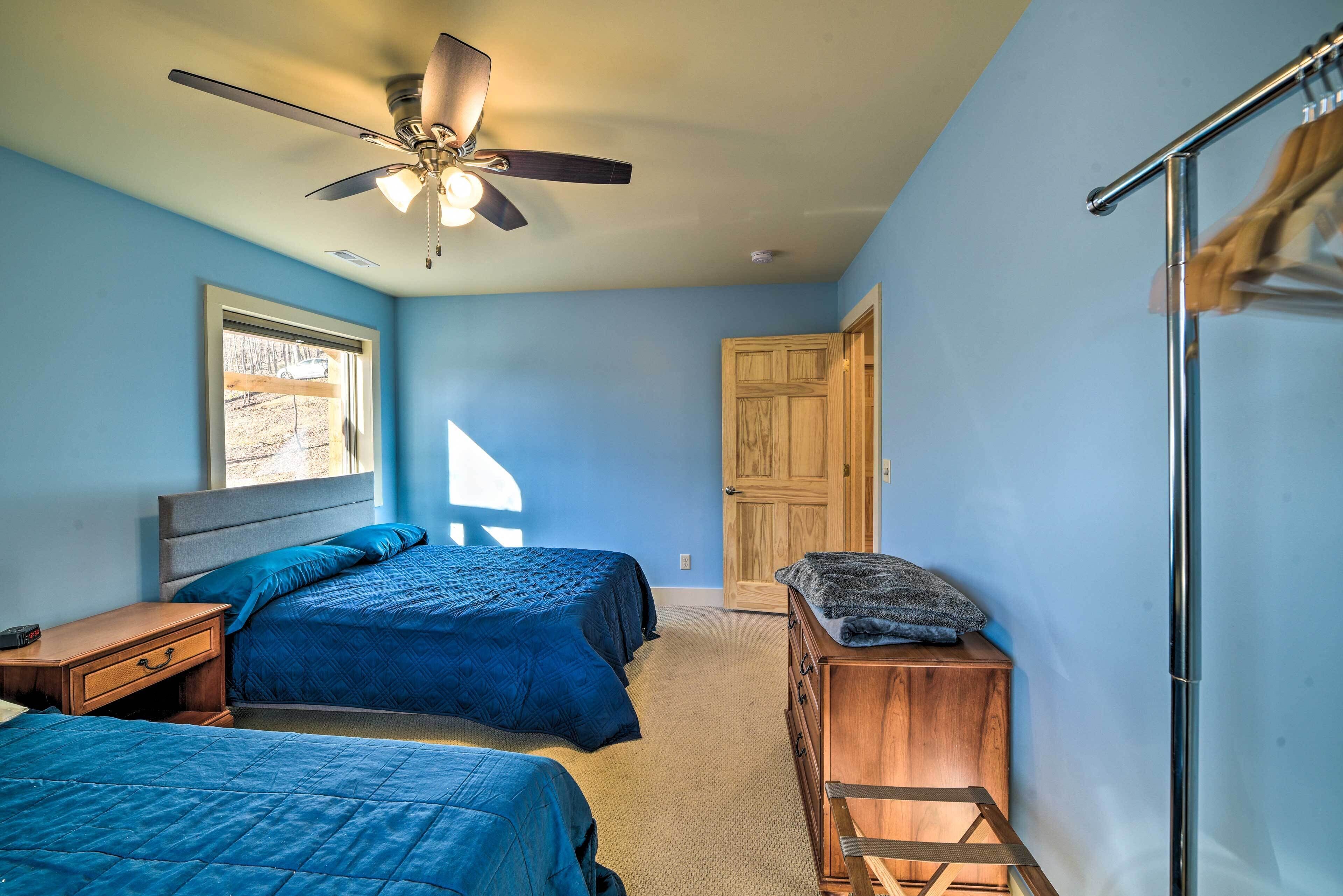 A bedroom with two beds, a ceiling fan, a wooden dresser, and a window with a view of trees.