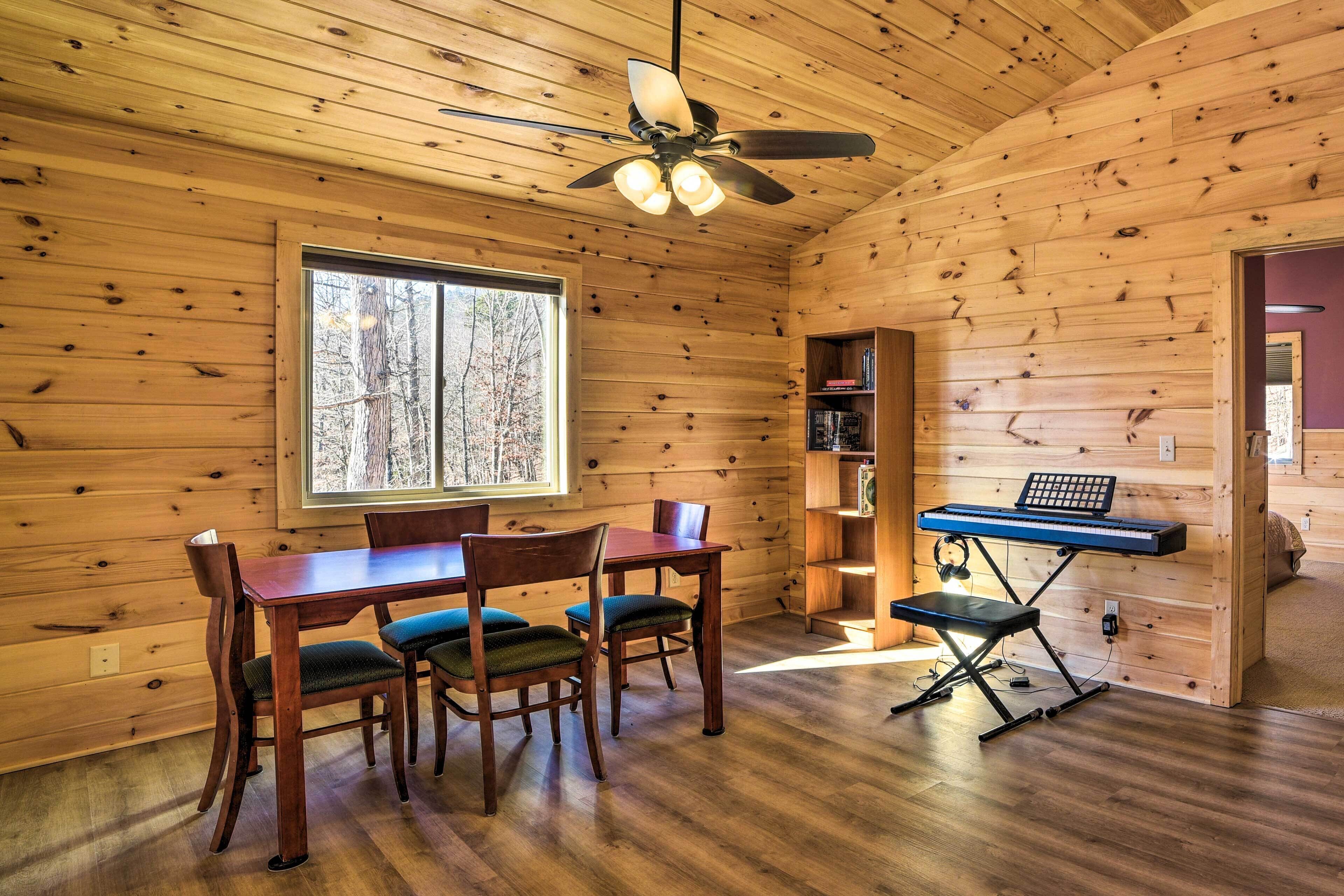 A wooden cabin interior with a dining table, chairs, a ceiling fan, and a keyboard on a stand.