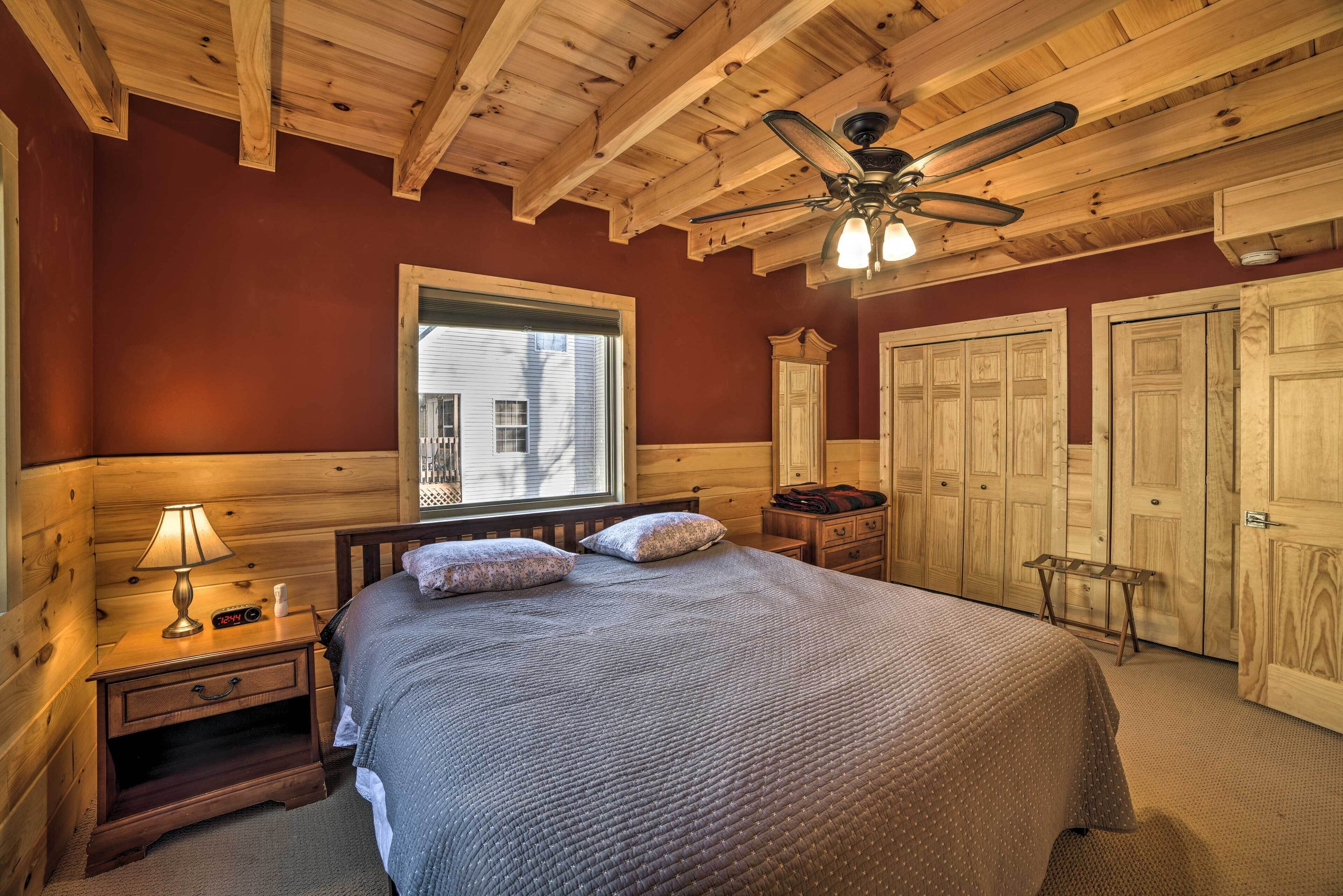 A bedroom with a wooden ceiling, a bed with a quilted blanket, a nightstand with a lamp, and a window with blinds.