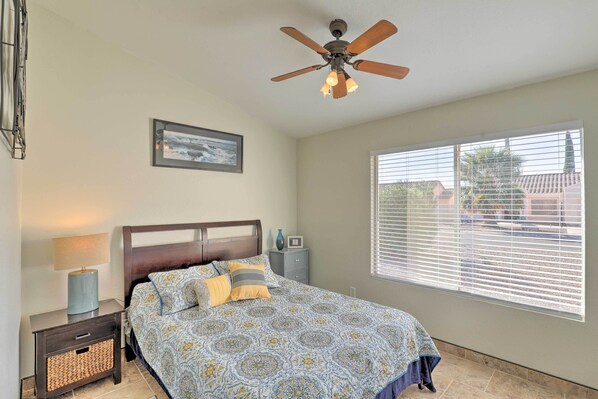 A bedroom with a bed, a ceiling fan, a nightstand, a lamp, a window with blinds, and a framed picture on the wall. - North Tucson Home w/ Patio by Catalina State Park! (Tucson)