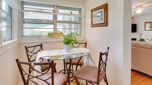 A dining area with a glass table, brown chairs, a potted plant, and a window with a welcome sign.