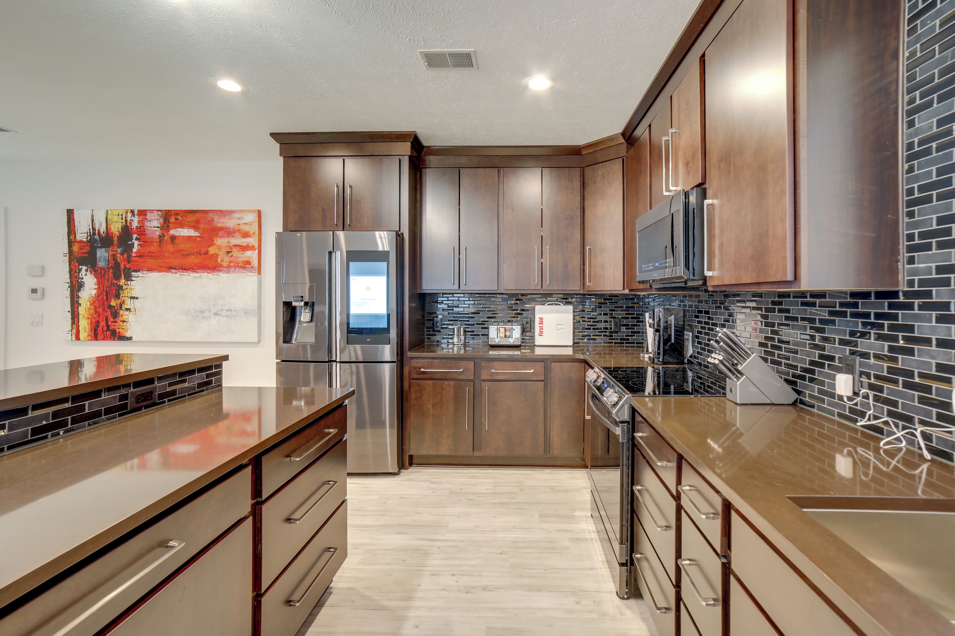 A modern kitchen with stainless steel appliances, wooden cabinets, and a black tiled backsplash.