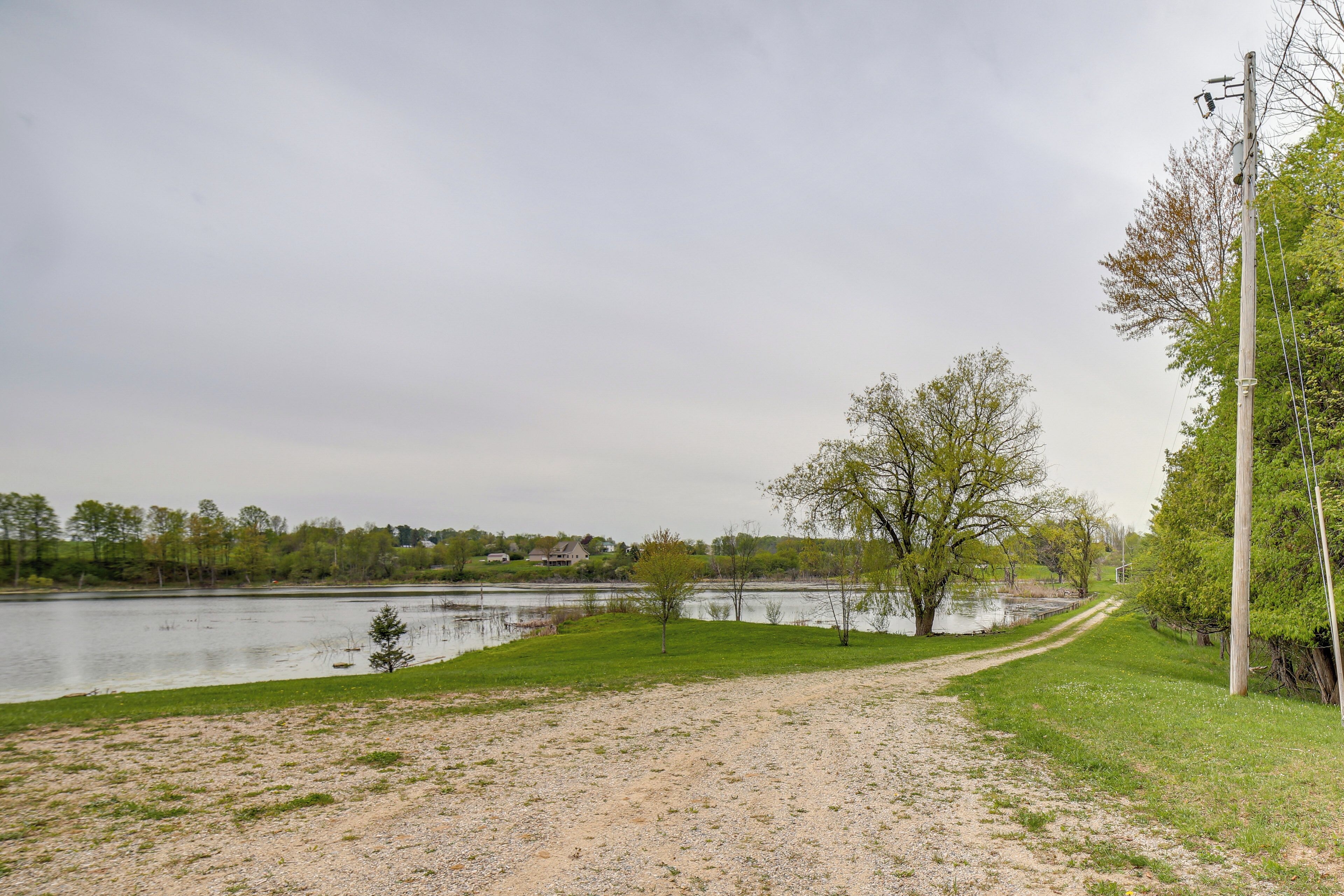 A gravel path leading to a body of water with trees and a utility pole.