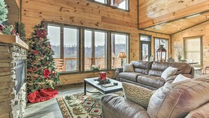 A cozy cabin-style room with a large window, a fireplace, a leather couch, and a Christmas tree. - Smoky Mountain Hideaway w/ Hot Tub, Deck & Views! (Gatlinburg)