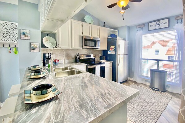 A modern kitchen with white cabinets, a marble countertop, and a built-in microwave.