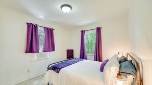 A bedroom with a bed, purple curtains, a window, and a bedside lamp. - Winston-salem Vacation Rental ~ 3 Mi to Downtown! (Winston-Salem)