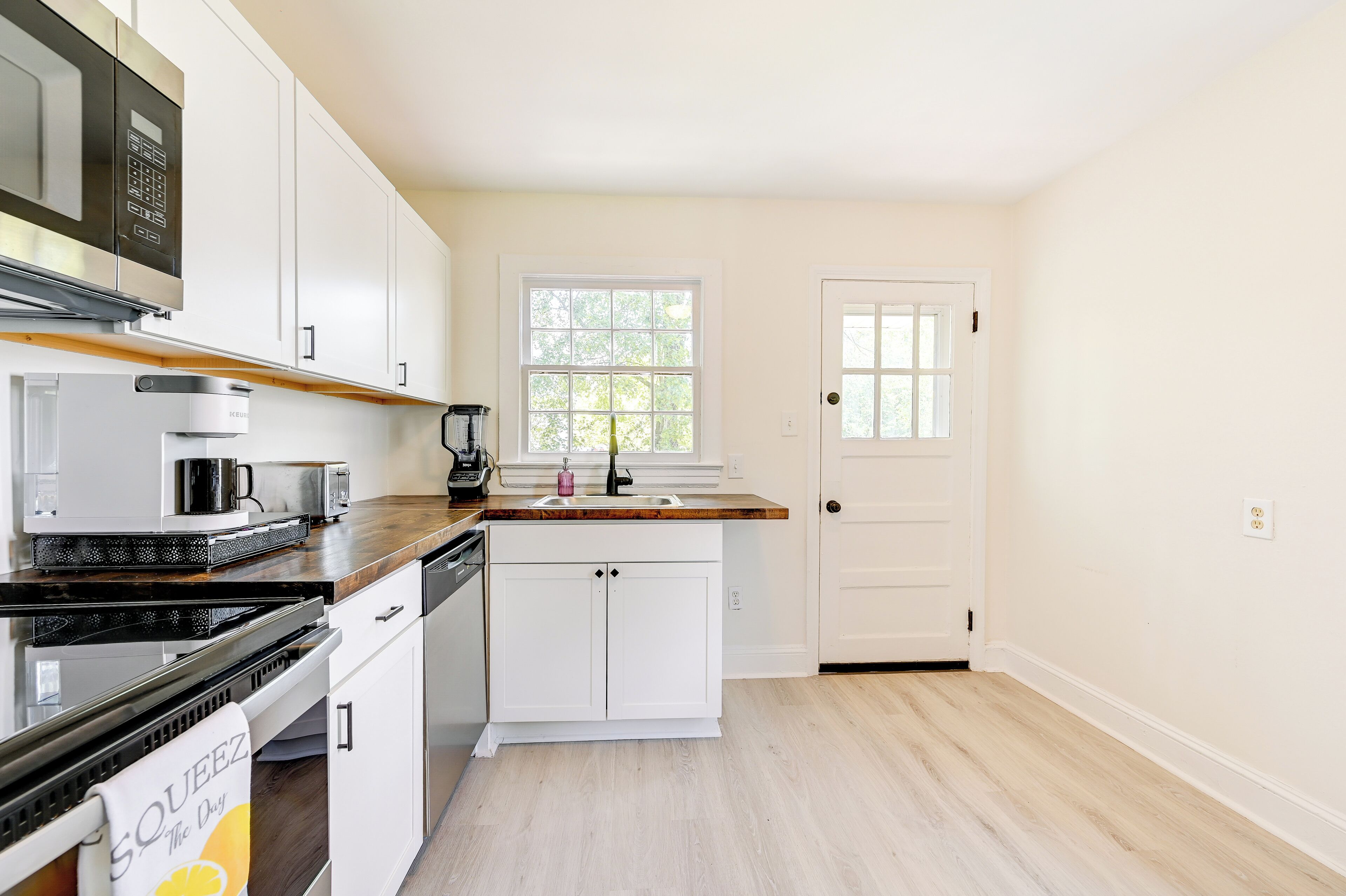 A modern kitchen with white cabinetry, a wooden countertop, a built-in oven, and a window with a view of trees.