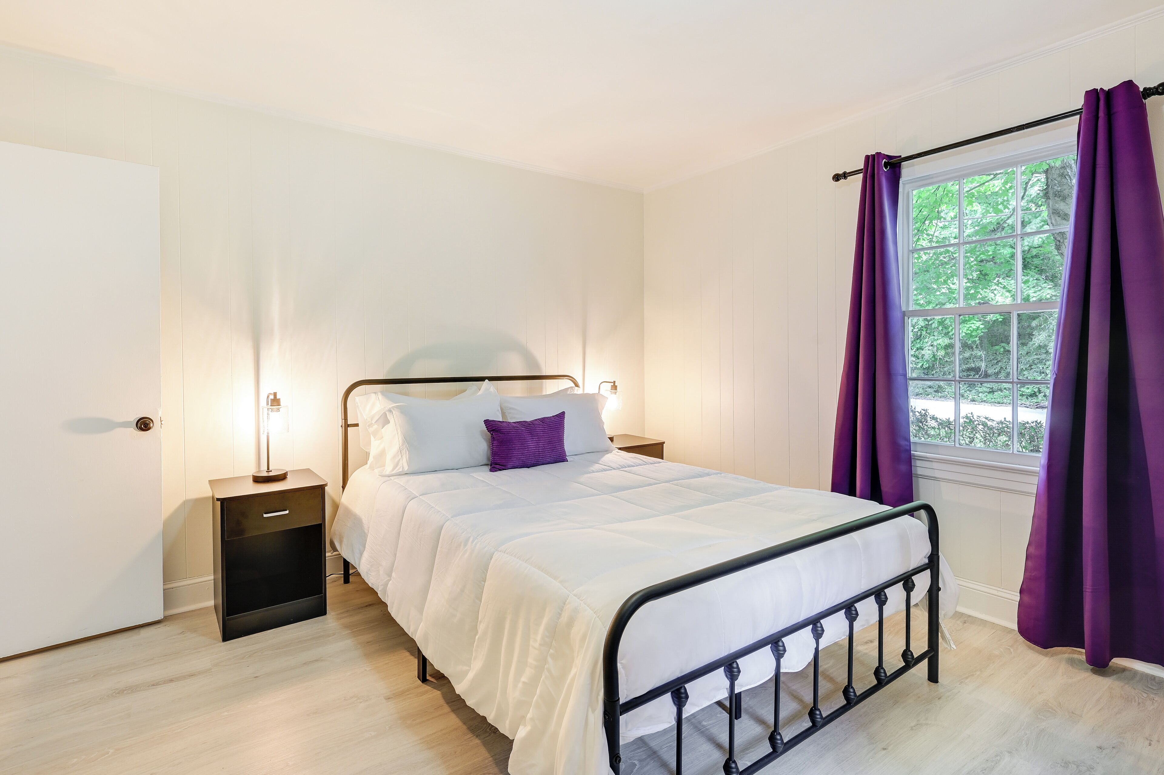 A bedroom with a bed, nightstands, a window with curtains, and a door.