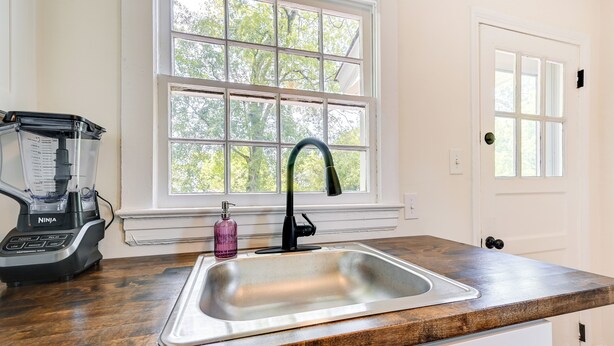 A kitchen with a stainless steel sink, a Ninja blender, and a window with a view of trees. - Winston-salem Vacation Rental ~ 3 Mi to Downtown! (Winston-Salem)