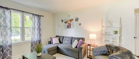 A living room with a sectional sofa, a small table, a chair, a lamp, and a bookshelf.