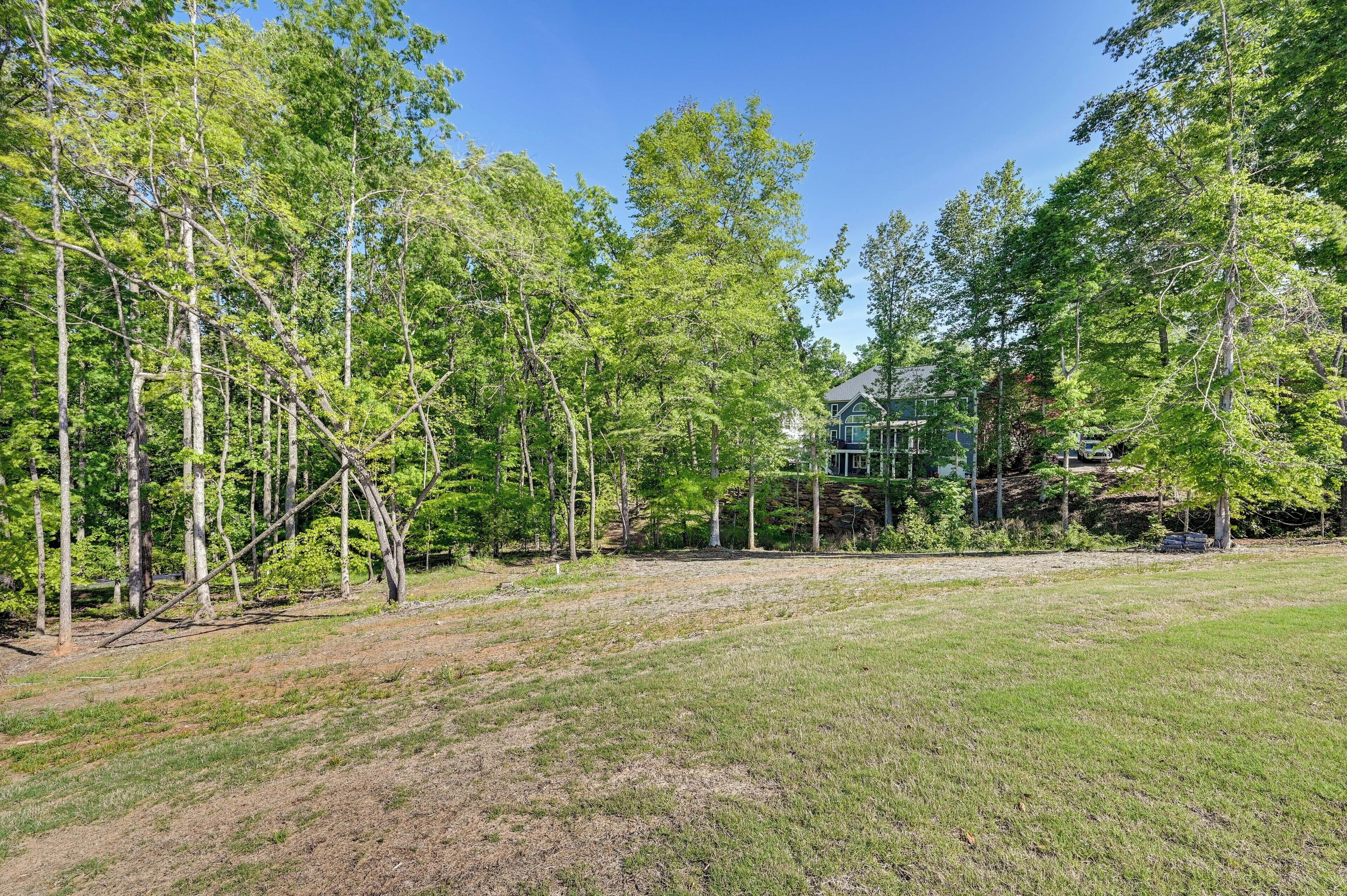 A large, open grassy area with tall trees and a house in the background.