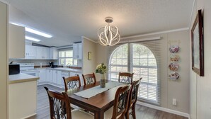 A dining area with a wooden table and chairs, a chandelier, and a large window with blinds. - Walk to Lake Chatuge! Hayesville Cabin w/ Fire Pit (Hayesville)