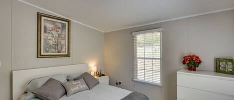 A bedroom with a bed, bedside table, lamp, window, dresser, and a framed picture on the wall.