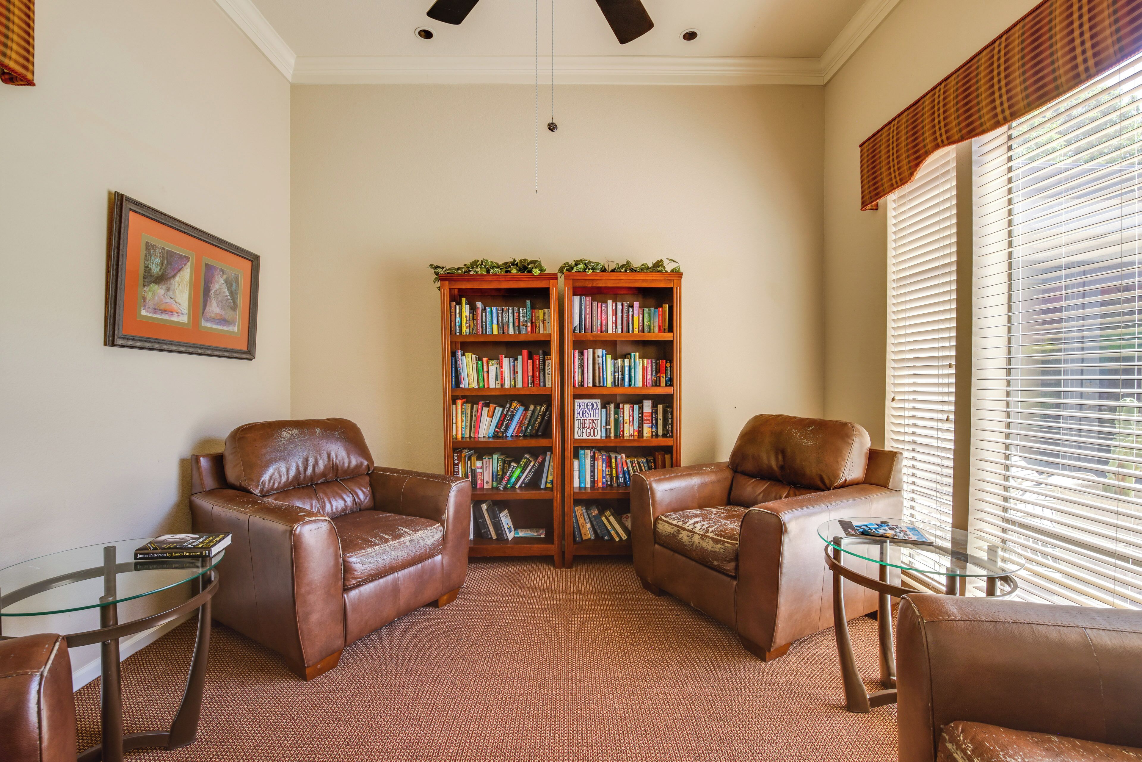 A living room with two leather armchairs, a glass coffee table, and a bookshelf filled with books.