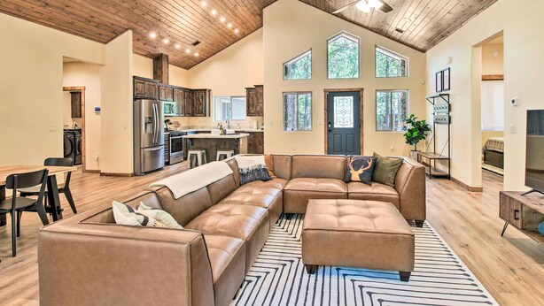 A spacious living area with a large L-shaped sectional sofa, a dining table with chairs, and a kitchen in the background. - Fire Pits, Spacious Yard: Wooded Pinetop Escape! (Pinetop)