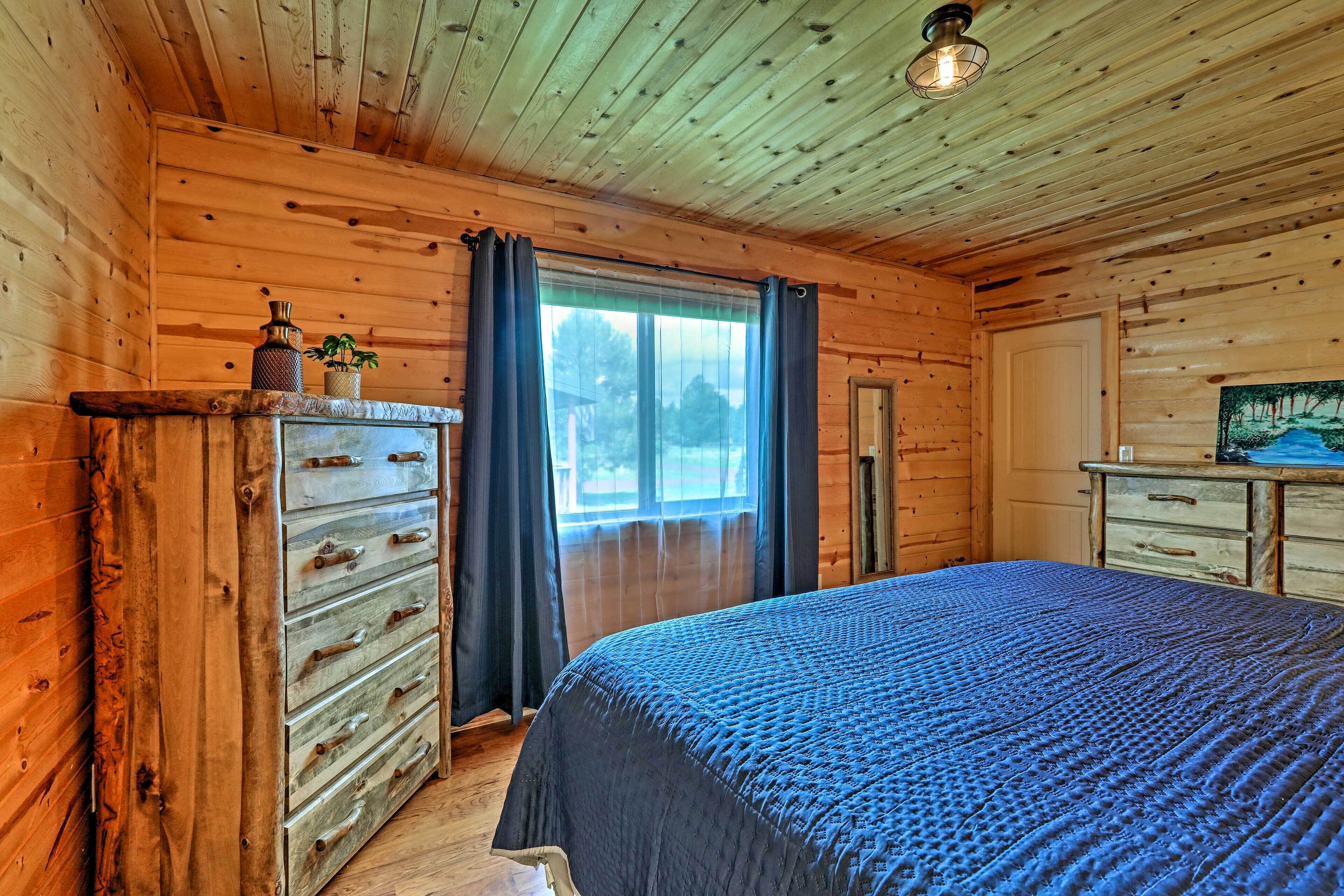 A wooden cabin bedroom with a bed, dresser, and a window with curtains.