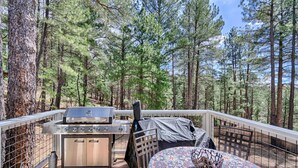 Une terrasse avec un barbecue et une table, entourée d’une forêt.