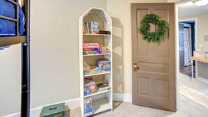 A room with a bunk bed, a white shelving unit with board games, and a door with a wreath. - Charming Negaunee Home ~ 2 Mi to Teal Lake! (Negaunee)