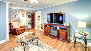 A living room with a wooden floor, a glass coffee table, a leather sofa, a TV, and a ceiling fan. - Charming Negaunee Home ~ 2 Mi to Teal Lake! (Negaunee)