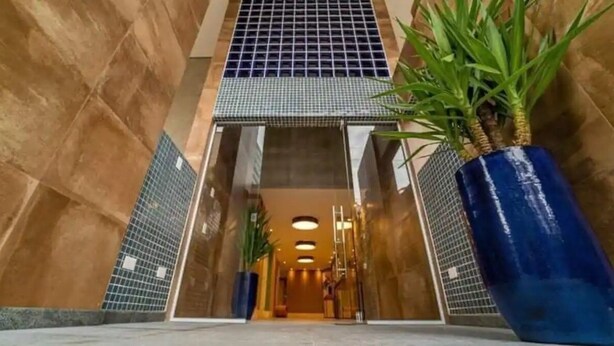 L’entrée d’un hôtel, avec un sol carrelé, un grand bac bleu contenant une plante et un portail en métal.