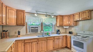 A kitchen with wooden cabinets, a white stove, a sink, and a window with a lace curtain. - Bonfires & Bbqs! Creekside Retreat in Marshall (Marshall)