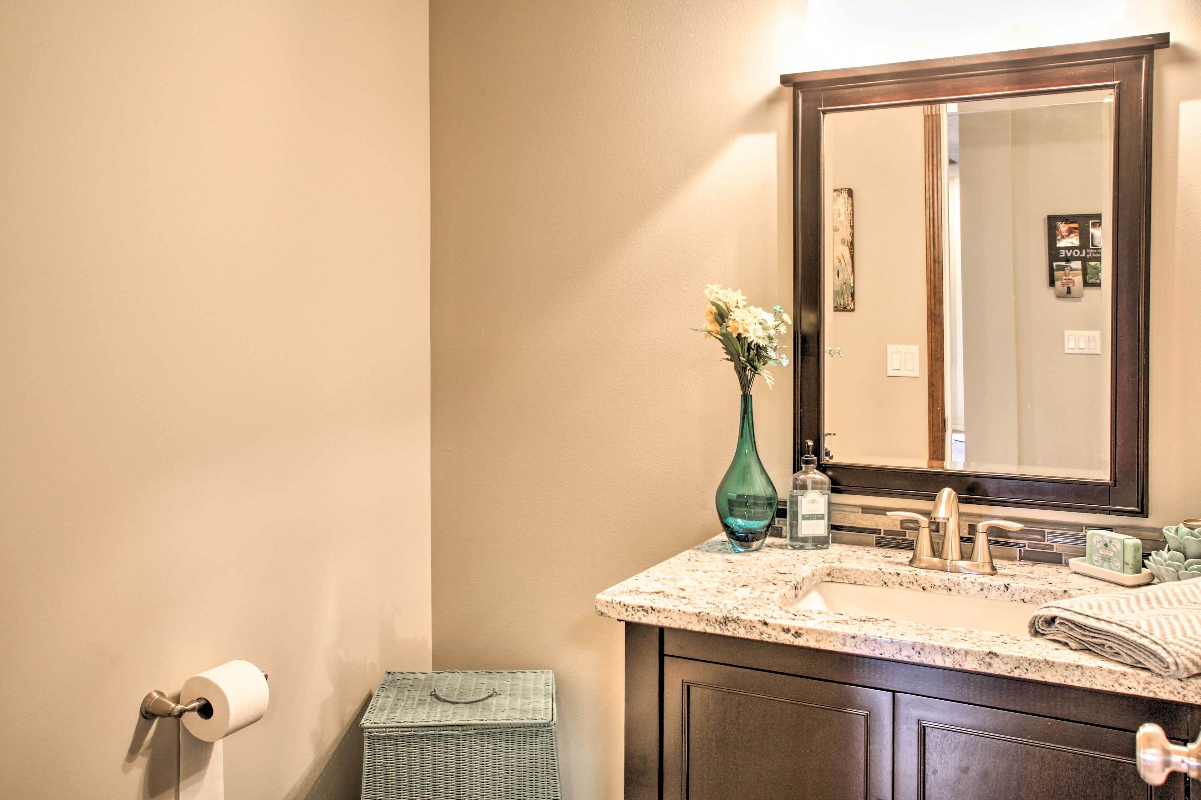 A bathroom with a marble sink, a mirror, a toilet paper holder, and a wicker basket.