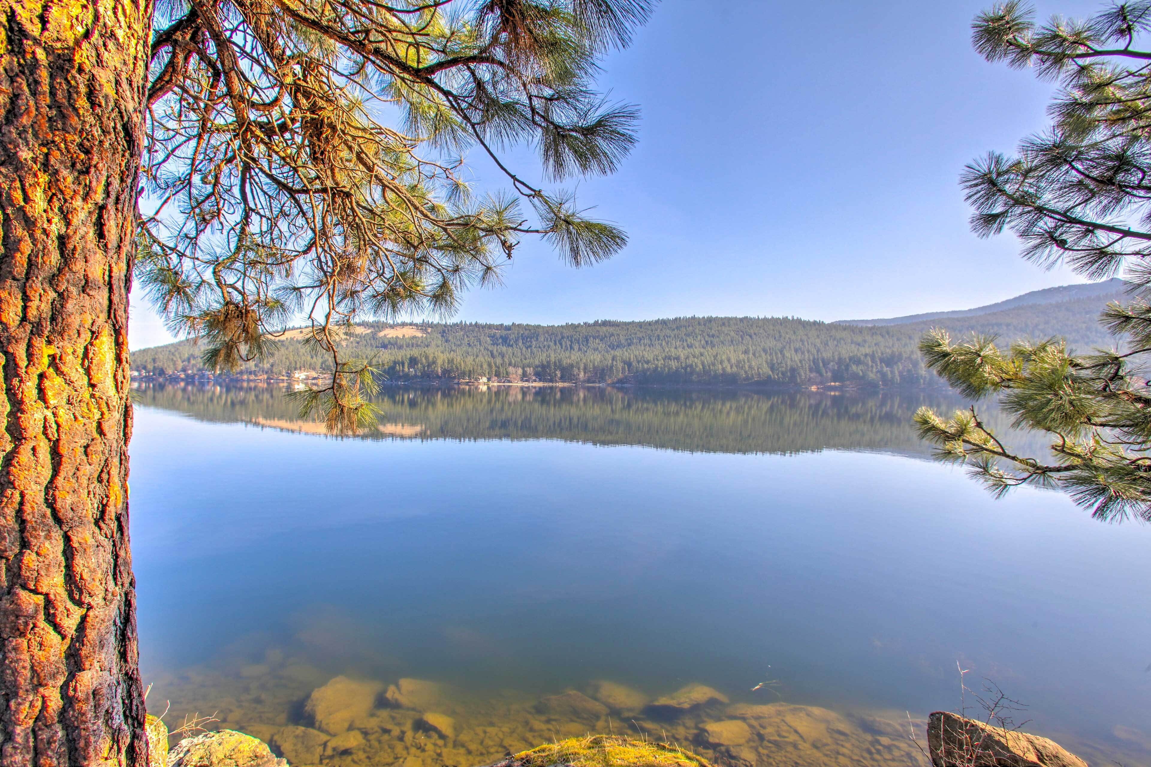 A calm lake with clear water, surrounded by dense forest and mountains in the background.