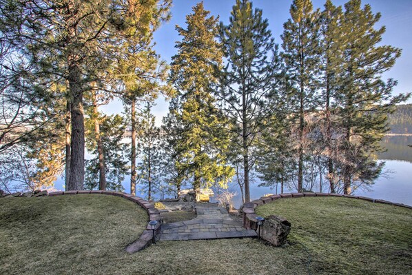 A stone pathway leading to a dock by a lake, surrounded by tall pine trees.