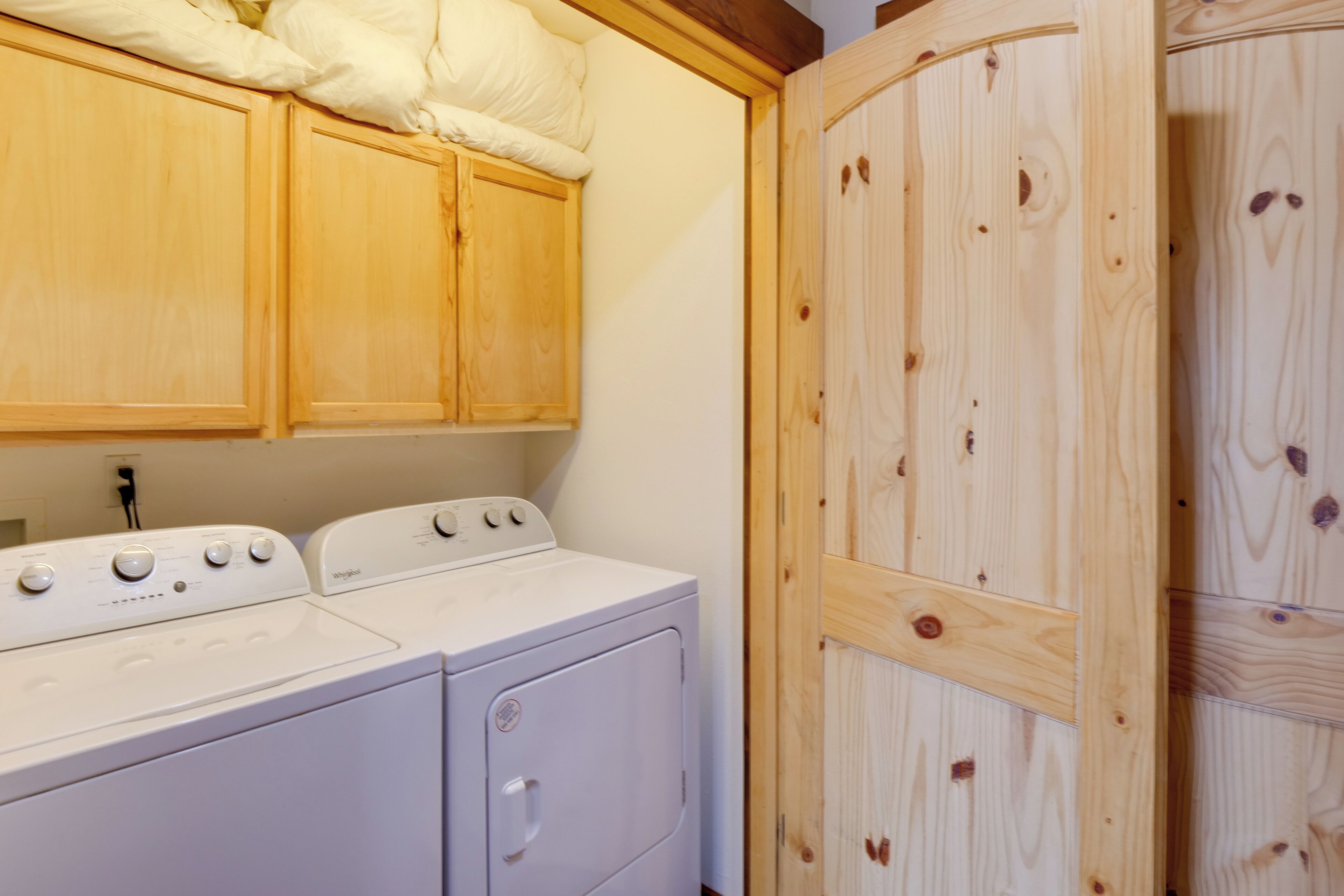 A laundry area with a front-loading washer and dryer, wooden cabinets, and a wooden wardrobe.