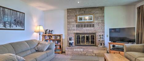 Ein Wohnzimmer mit Kamin aus Stein, einem Fernseher und einem Bücherregal.