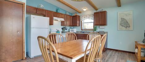 A kitchen with wooden cabinets, a white refrigerator, a dining table with chairs, and a chandelier.