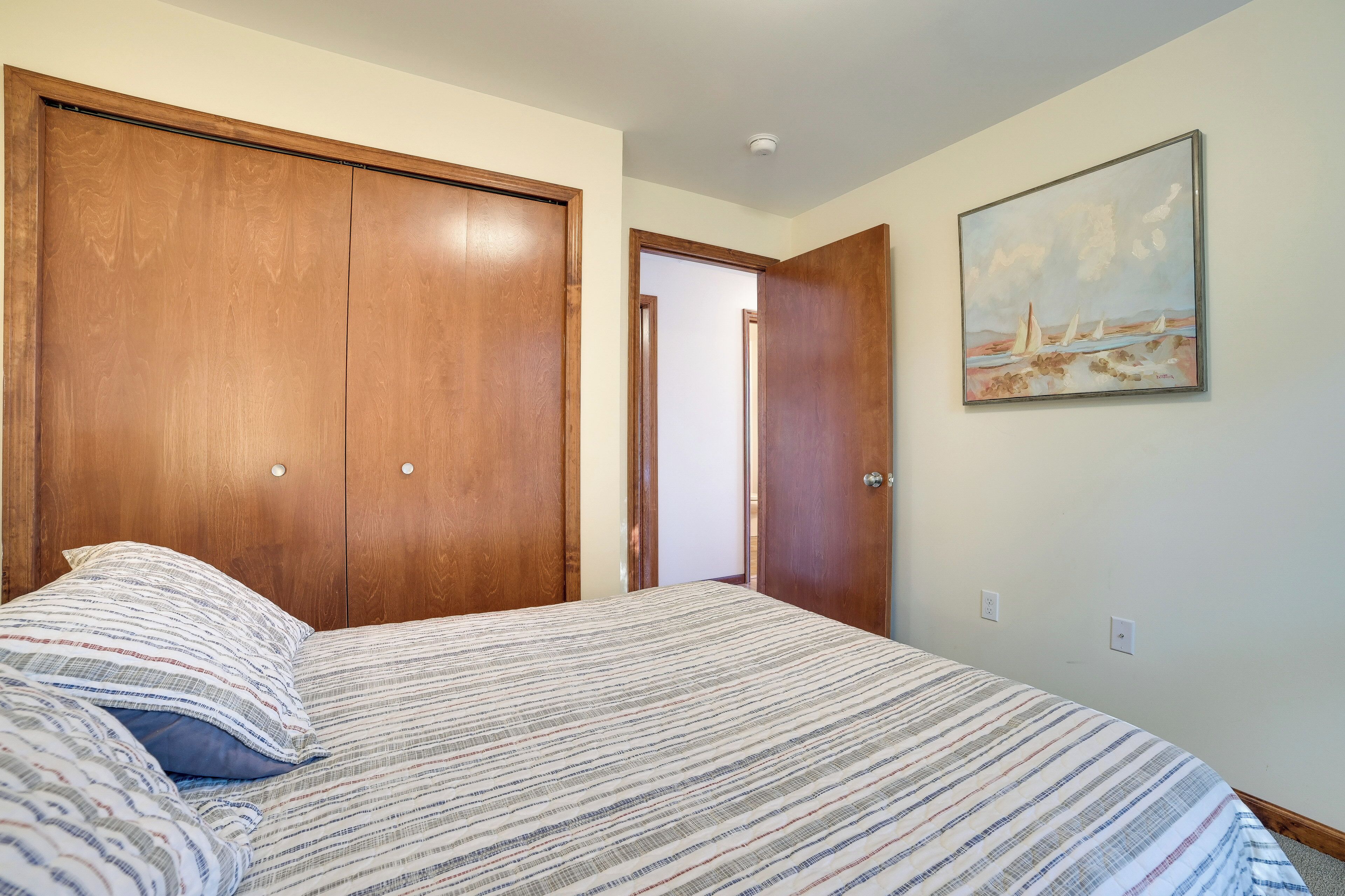 Een slaapkamer met een bed, een houten garderobe en een schilderij aan de muur.