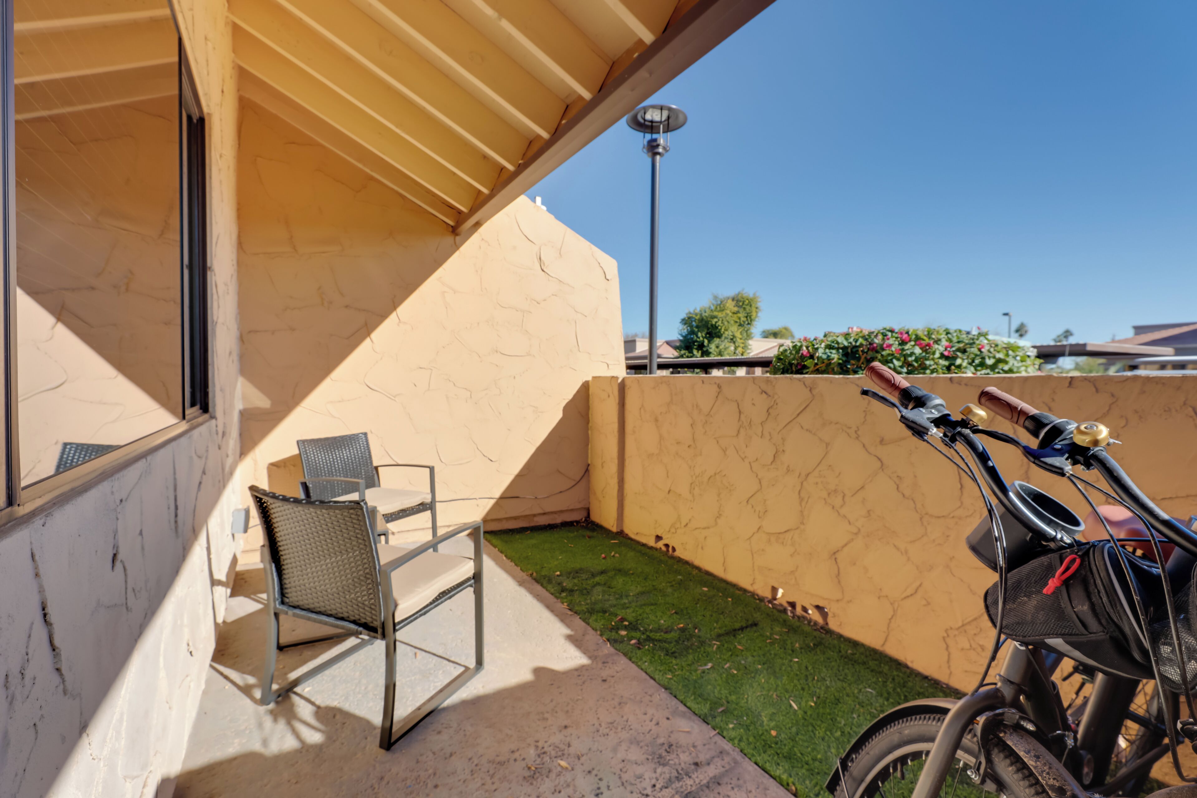 A patio area with a table and chairs, a bicycle, and a small patch of artificial grass.