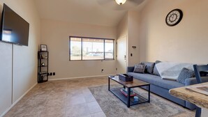 A living room with a flat-screen TV, a sofa, a coffee table, and a window with blinds. - Scottsdale Loft Near Golf Course & Old Town! (Scottsdale)