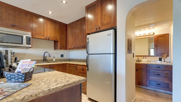 A kitchen with wooden cabinets, a stainless steel refrigerator, a microwave, and a granite countertop. - Scottsdale Loft Near Golf Course & Old Town! (Scottsdale)