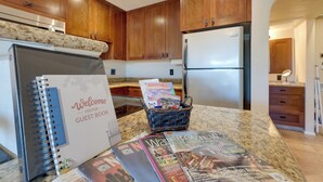 A kitchen with wooden cabinets, a granite countertop, a refrigerator, and a welcome guest book. - Scottsdale Loft Near Golf Course & Old Town! (Scottsdale)