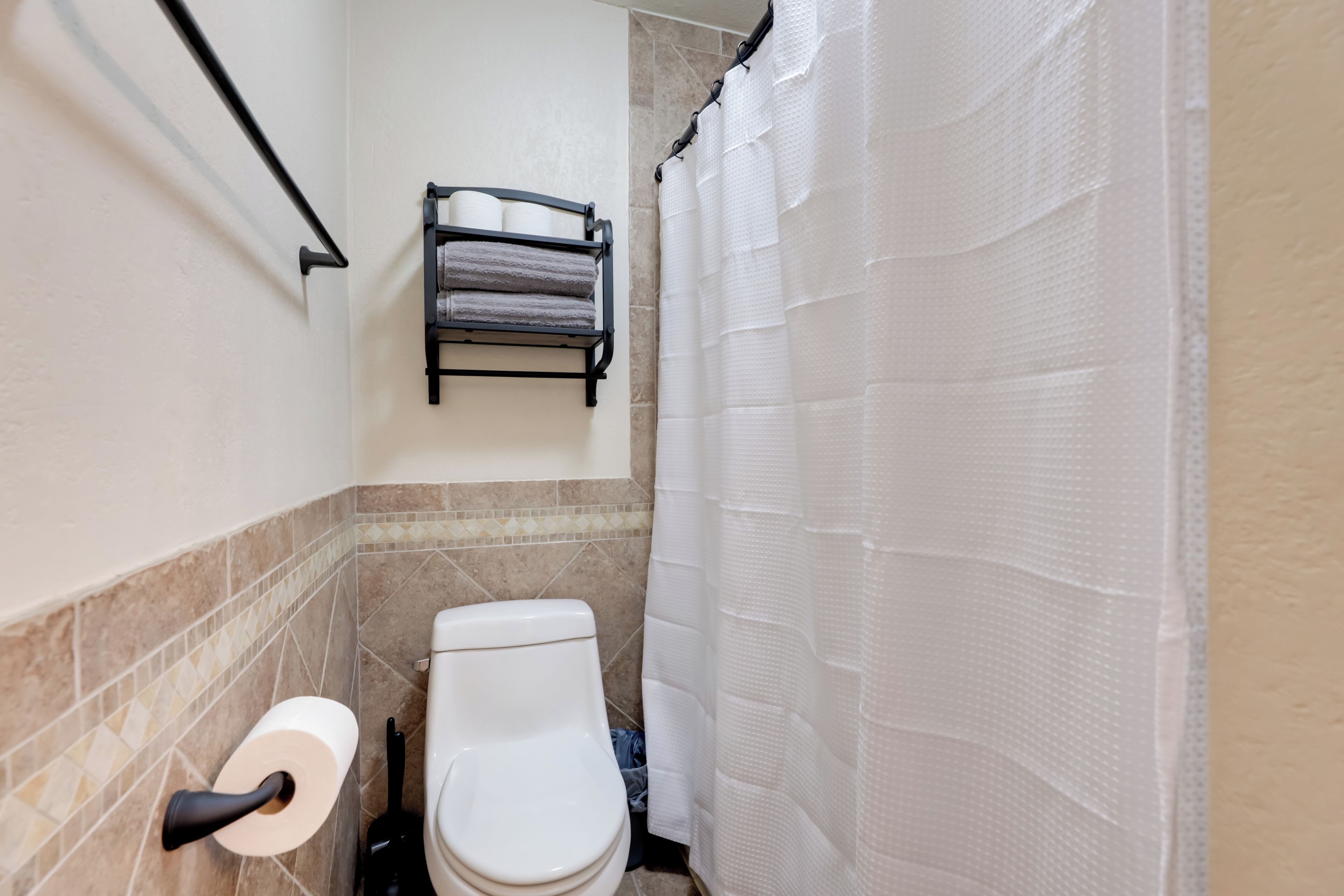 Un baño con inodoro, toallero con toallas, dispensador de papel higiénico y cortina de ducha.