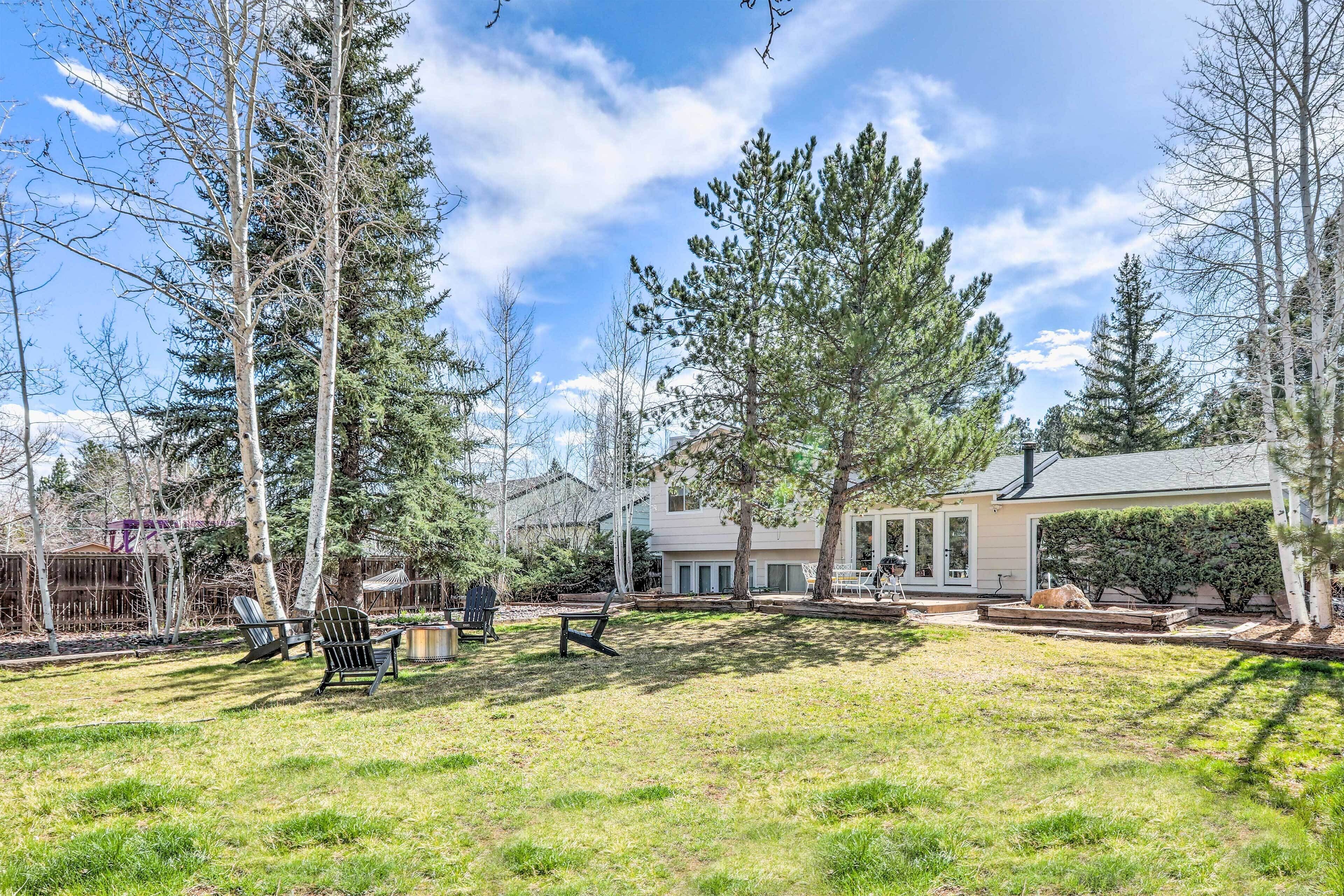 A backyard with a lawn, two Adirondack chairs, a dogwood tree, and a house with a covered patio.
