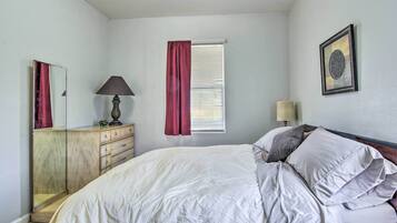 A bedroom with a bed, a dresser, a window with curtains, a lamp, and a framed picture on the wall.